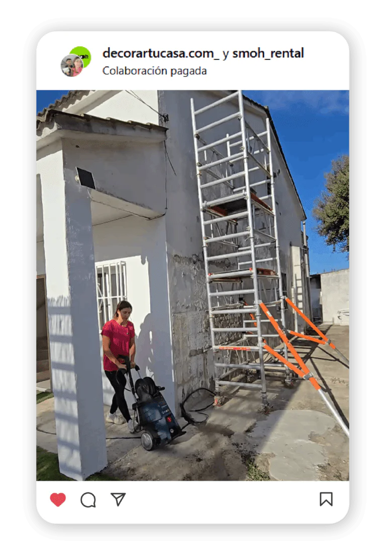 White building under renovation with metal scaffolding and orange safety rails; a person with a stroller nearby.