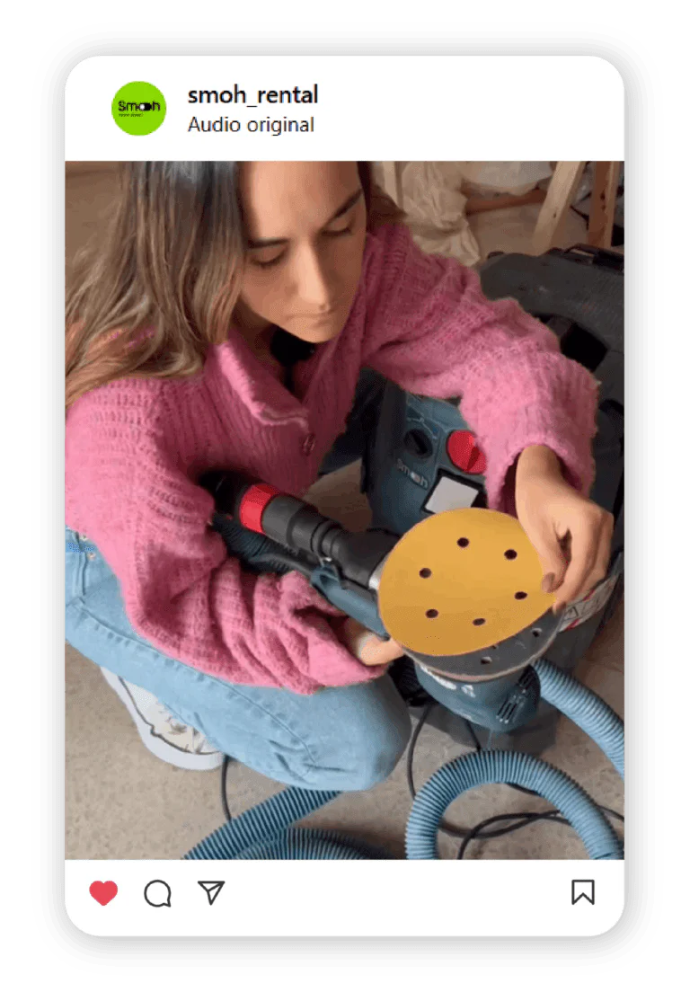 Person in a pink sweater operating a blue power drill with a yellow circular guard indoors, dust hose nearby