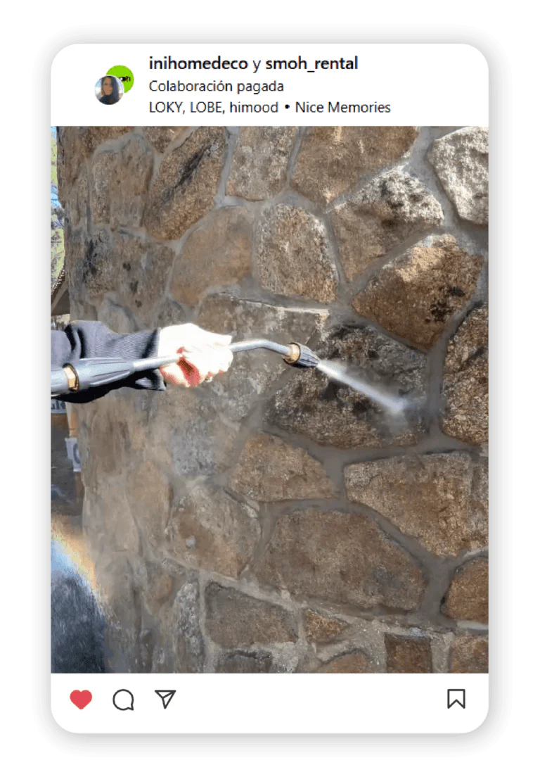 Person in a dark sleeve uses a pressure washer to spray water on a textured stone wall outdoors.