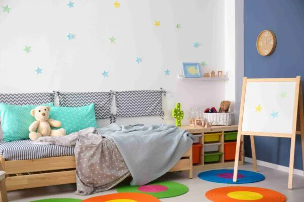 Children's bedroom with a star-decorated wall, bed, teddy bear, and colorful circular rugs; an easel and toy storage in the corner.